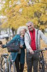 Portrait smiling, carefree senior couple with bicycles in autumn park — Stock Photo
