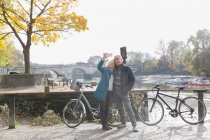 Casal sênior com bicicletas tirando selfie no rio outono — Fotografia de Stock