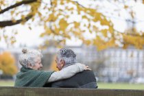 Sans soucis, affectueux couple de personnes âgées étreignant sur le banc dans le parc d'automne — Photo de stock