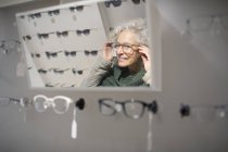 Senior woman trying on eyeglasses in optometry shop — Stock Photo