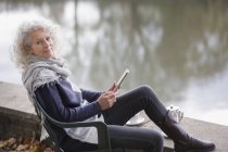Portrait confident active senior woman using digital tablet at park pond — Stock Photo