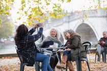 Woman with digital camera photographing active senior women friends at autumn park cafe — Stock Photo