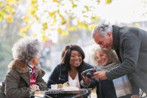 Active senior friends using digital camera at autumn sidewalk cafe — Stock Photo