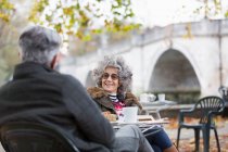 Active senior couple talking, enjoying coffee at autumn park cafe — Stock Photo