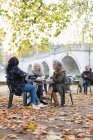 Smiling active senior women friends enjoying coffee at autumn park cafe — Stock Photo