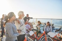 Активний старший друг туристів з велосипедами, що їдять морозиво на сонячному березі океану — стокове фото