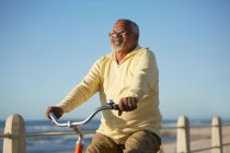 Carefree active senior man tourist bike riding along ocean — Stock Photo