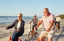 Active senior tourist friends bike riding on sunny boardwalk along ocean — Stock Photo