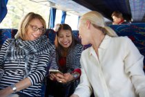 Улыбаясь активным старшим друзьям-туристам с помощью смартфона в автобусе — стоковое фото