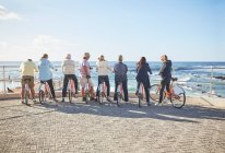 Активные старшие друзья-туристы на велосипедах смотрят на солнечный вид на океан — стоковое фото