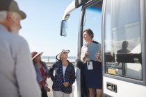 Экскурсовод беседует с активными пожилыми туристами у дверей туристического автобуса — стоковое фото