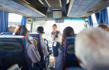 Guia turístico feminino com microfone conversando com turistas seniores ativos no ônibus turístico — Fotografia de Stock