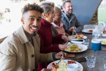 Portrait smiling young man eating breakfast with friends at restaurant outdoor patio — Stock Photo