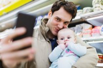 Affectionate father and baby daughter taking selfie in supermarket — Stock Photo