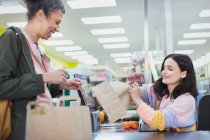 Female cashier helping customer bag groceries at supermarket checkout — Stock Photo