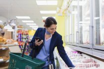 Frau mit Smartphone im Supermarkt einkaufen — Stockfoto