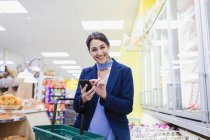 Retrato sonriente, mujer segura con compras de teléfonos inteligentes en el supermercado - foto de stock