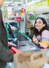 Friendly female cashier helping customer at supermarket checkout — Stock Photo