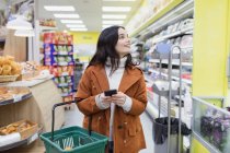 Mujer con compras de teléfonos inteligentes en el supermercado - foto de stock