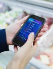 Закрыть женщину с помощью цифрового списка покупок на смартфоне в супермаркете — стоковое фото