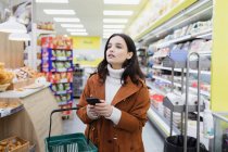 Femme avec téléphone intelligent faisant du shopping dans un supermarché — Photo de stock