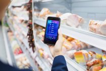 Frau benutzt digitale Einkaufsliste auf Kameratelefon im Supermarkt — Stockfoto