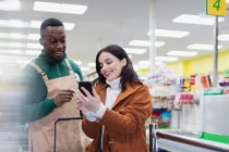 Tienda de comestibles ayudando al cliente con el teléfono inteligente en el supermercado - foto de stock