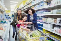 Playful multi-generation women pushing shopping cart in supermarket aisle — Stock Photo