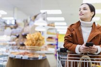 Mulher com telefone inteligente compras no supermercado — Fotografia de Stock