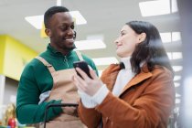 Negozio alimentare aiutare il cliente con smart phone nel supermercato — Foto stock