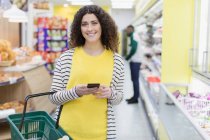 Портрет улыбается, уверенная женщина со смартфоном покупки в супермаркете — стоковое фото