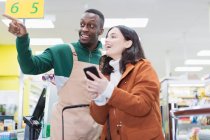 Männlicher Lebensmittelhändler hilft Kundin im Supermarkt — Stockfoto