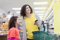 Mãe e filha com telefone inteligente compras no supermercado — Fotografia de Stock