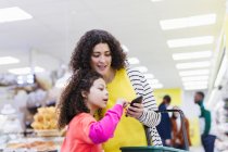 Madre e hija con compras de teléfonos inteligentes en el supermercado - foto de stock