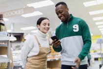 Grocer ajudando o cliente com telefone inteligente no supermercado — Fotografia de Stock