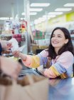 Smiling, friendly female cashier giving receipt to customer at supermarket checkout — Stock Photo