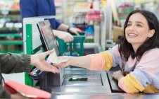 Улыбающаяся кассирша выдаёт квитанцию клиенту на кассе супермаркета — стоковое фото
