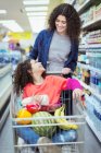Happy mother pushing daughter in shopping cart in supermarket — Stock Photo