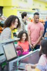 Cashier helping mother and daughter at supermarket checkout — Stock Photo