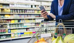 Mujer con compras de teléfonos inteligentes en el supermercado - foto de stock