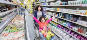 Mother pushing playful daughter in shopping cart in supermarket aisle — Stock Photo