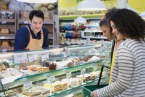 Arbeiter hilft Kunden in Bäckereivitrine im Supermarkt — Stockfoto