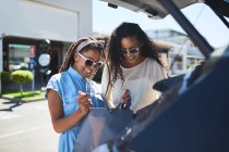 Women looking into shopping bags in sunny parking lot — Stock Photo