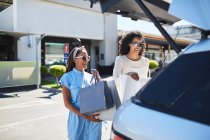 Women loading shopping bags into back of car in sunny parking lot — Stock Photo