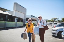 Happy senior women with shopping bags in sunny parking lot — Stock Photo