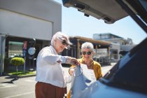 Donne anziane amiche che caricano borse della spesa nel retro dell'auto nel parcheggio soleggiato — Foto stock