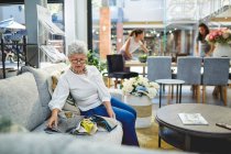 Seniorin betrachtet Stoffmuster auf Sofa im Dekorationsgeschäft — Stockfoto