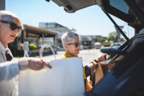 Старші жінки завантажують сумки в задню частину автомобіля на сонячній парковці — стокове фото