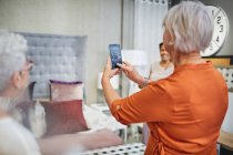 Femme avec téléphone intelligent photographier lit dans la maison boutique de décoration — Photo de stock