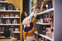 Mulher ajudando cliente sênior chegar para frigideira na loja de produtos domésticos — Fotografia de Stock